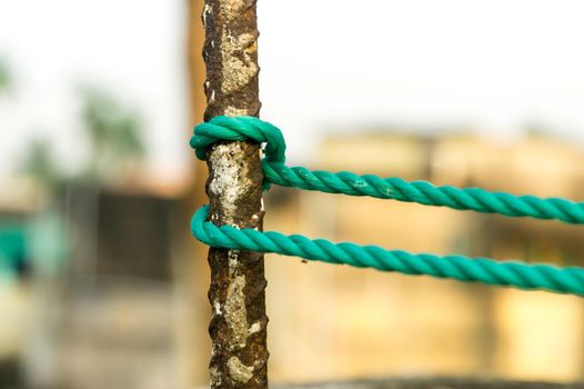 A rope is tied in a knot around a fence post, rope tied Hitch Knots on a rusty iron pole isolated from background.