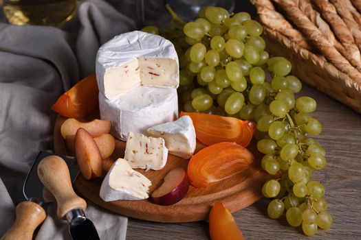 Cheese camembert with white grapes, sliced persimmons and plums, a great appetizer for wine 