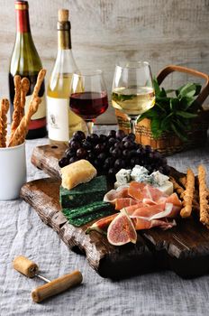 Dishes for a snack Antipasto on a wooden board with prosciutto, different kinds of cheese, grapes and figs on a table with wine