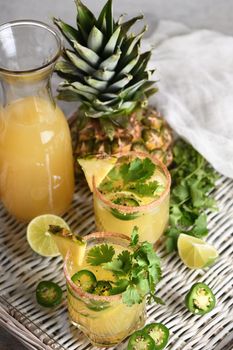 Spicy pineapple margarita with jalapeno slices, lime and cilantro sprigs