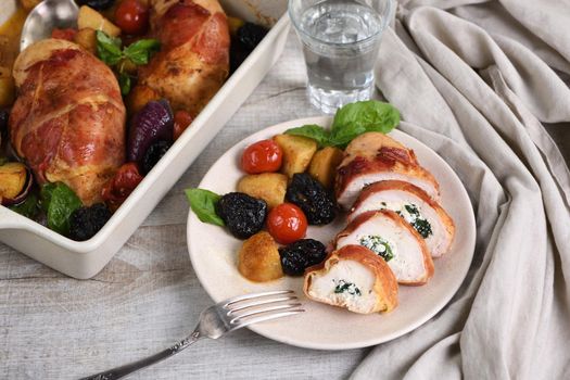 Sliced ​​chicken breast stuffed with goat cheese with spinach, wrapped in prosciutto, with a side dish of baked potatoes, tomato and dried prunes