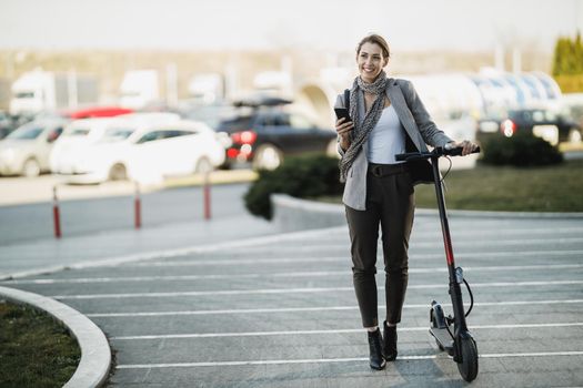 A young businesswoman with an electric push scooter going to work and using a smartphone.