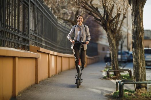 A young businesswoman riding an electric scooter on her way to work through the city.