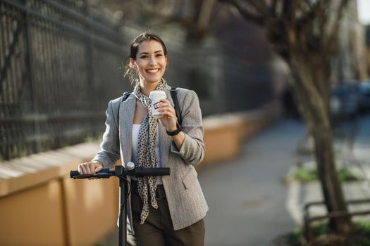 A young businesswoman drinking coffee during go to work with an electric scooter.