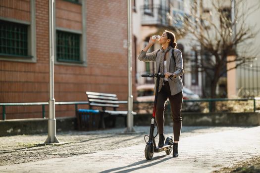 A young businesswoman drinking coffee during go to work with an electric scooter.