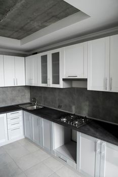 Modern minimalism style kitchen interior in monochrome tones. Custom kitchen with grey white facadesmdf and dark grey countertop with installed kitchen hood and sink. Modular kitchen from chipboard