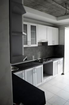 Modern minimalism style kitchen interior in monochrome tones. Custom kitchen with grey white facadesmdf and dark grey countertop with installed kitchen hood and sink. Modular kitchen from chipboard