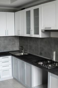 Modern minimalism style kitchen interior in monochrome tones. Custom kitchen with grey white facadesmdf and dark grey countertop with installed kitchen hood and sink. Modular kitchen from chipboard