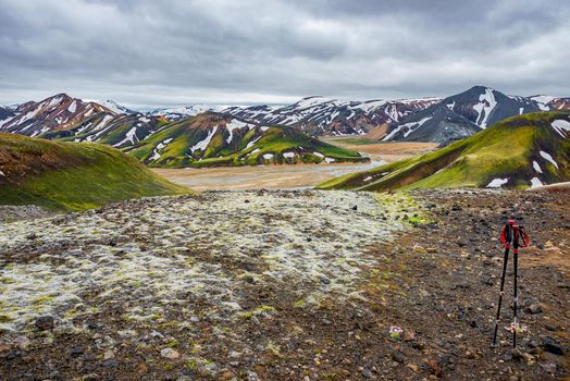 Majestic Icelandic landscape of colorful rainbow volcanic Landmannalaugar mountains, volcanic craters at famous Laugavegur hiking trail with dramatic sky, and hiking sticks in Iceland