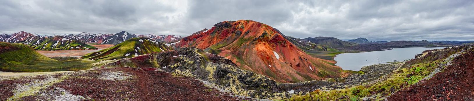 Panoramic surreal Icelandic landscape of colorful rainbow volcanic Landmannalaugar mountains, volcanic craters at famous Laugavegur hiking trail with dramatic sky, and Frostastadavatn lake in Iceland