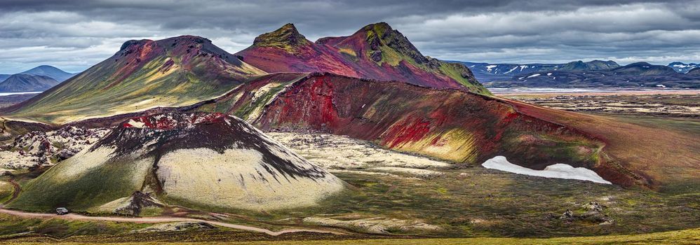 Panoramic surreal magic Icelandic landscape of colorful rainbow volcanic Landmannalaugar mountains, red and pink volcanic crater Stutur at famous Laugavegur hiking trail with dramatic sky and a big 4WD car on the road, Iceland