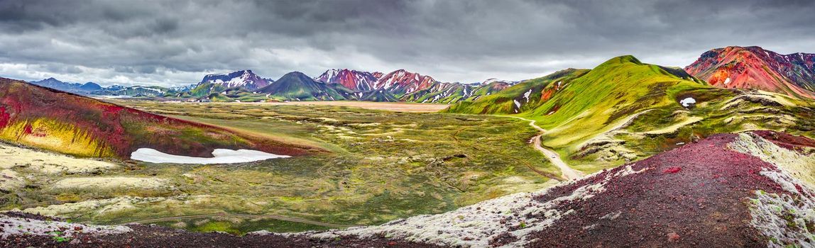 Panoramic unreal magic Icelandic landscape view of colorful rainbow volcanic Landmannalaugar mountains, red and pinky volcanic crater and famous Laugavegur hiking trail with dramatic sky, Iceland