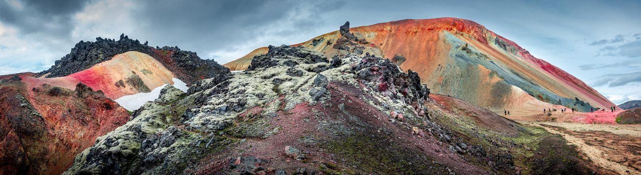 Panoramic landscape view of colorful rainbow volcanic Landmannalaugar mountains and famous Laugavegur hiking trail, with dramatic sky and snow in Iceland