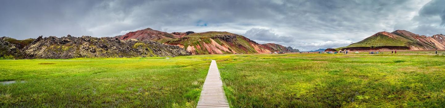 Panoramic view of colorful volcanic Landmannalaugar mountains, camping site and trail path at dramatic sky in Iceland