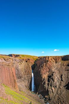 Beautiful and tall Icelandic waterfall Hengifoss and hiking trail to it, Iceland, sunny day, blue sky