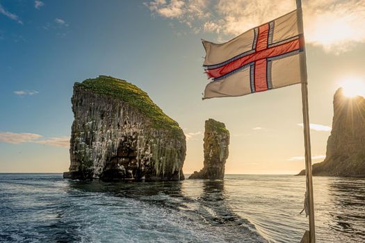 Sailing at mythical Faroe Islands full of seabirds during wonderful sunset and under Faroe Islands national flag, summer
