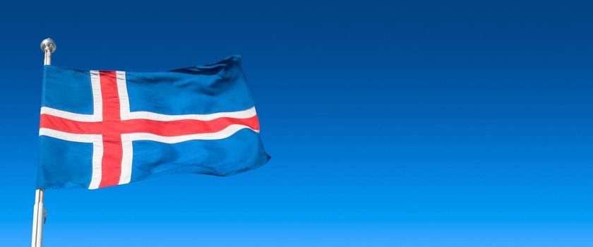 Banner with blue Icelandic national civil flag with red and white cross at blue sky background with copy space for text