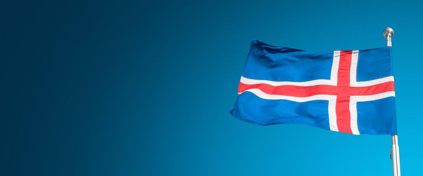 Banner with blue Icelandic national civil flag with red and white cross at blue sky background with copy space for text