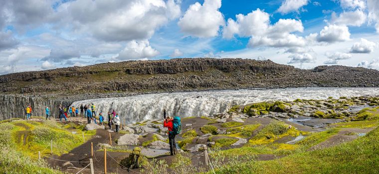 Panoramic view over biggest and most powerful waterfall in Europe called Dettifoss in Iceland, near lake Myvatn, with dramatic sky and tourists
