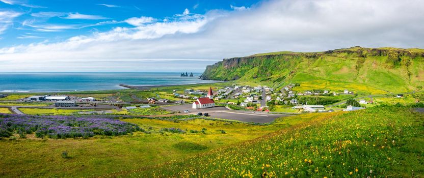 Panoramic view of basalt stacks Reynisdrangar, black sand beach, church and city of Vik at South Iceland