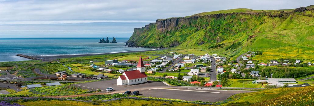 Panoramic view of basalt stacks Reynisdrangar, black sand beach, church and city of Vik at South Iceland