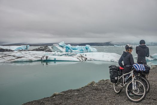 Two cyclists with mountain bikes standing at Glacier Lagoon Jokulsarlon with icebergs in Iceland
