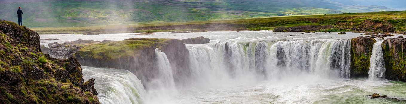 Panoramic view over powerful waterfall Godafoss with a lonely traveler standing at its cliff, Iceland
