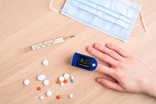 Person using pulse oximeter device near to pills, thermometer and medical mask, healthcare monitoring concept