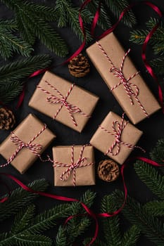 Christmas holidays composition. Red ribbon, eco gift boxes, pine cones and fir-tree.