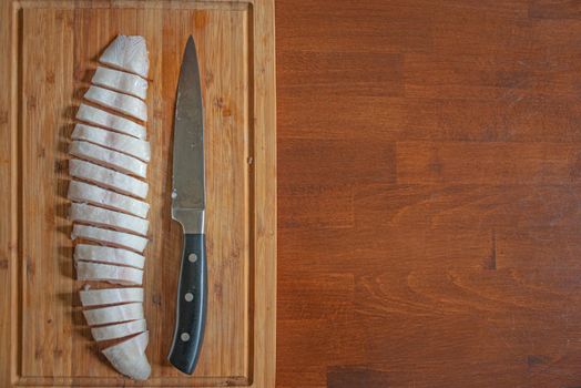 Half frozen fish at a wooden board cut on fine slices by a big knife, details, closeup, with copy space as a wooden table plate. Concept home cooking and healthy food
