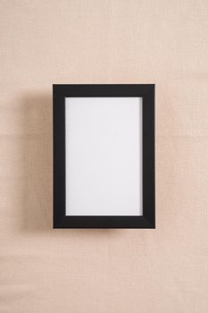 Black picture frame with white mockup on a beige textile