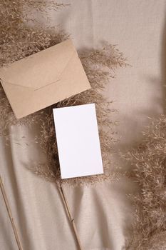 White blank paper card and envelope mockup with pampas dry grass on a beige neutral colored textile