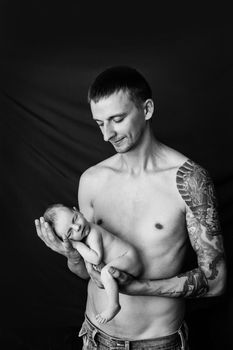 Father with tattoo on his arm is holding his newborn baby on a black and white background. High quality photo