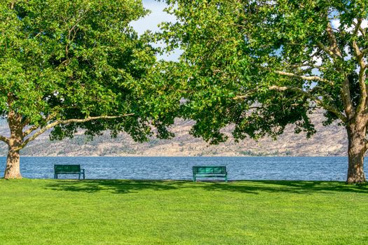 Lake shore sidewalk with green benches at the waterfront on Okanagan lake in British Columbia.