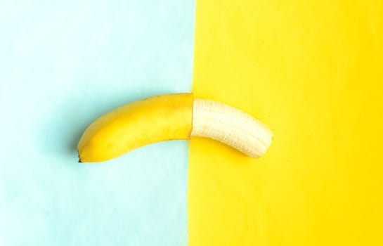 Partially peeled banana on blue yellow background.Tropic summer fruit