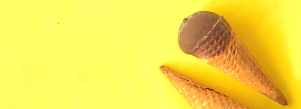 Top view, chocolate ice-cream cone on sunny summer yellow background, copyspace.Refreshing sweet delicacy for bright summer.