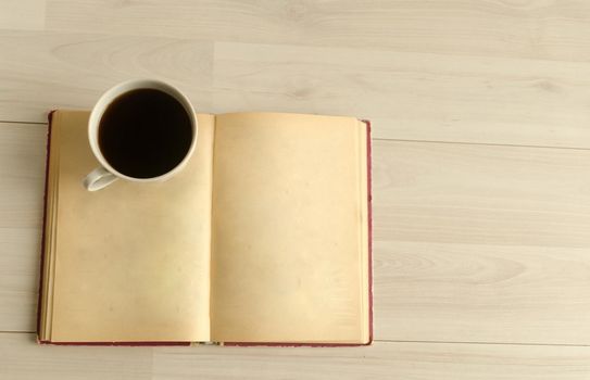 a cup of coffee and an open book on white wooden background