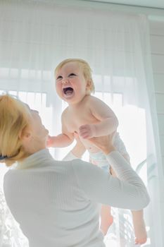 Mom, entertaining the baby, throws him up, rejoicing and having fun.