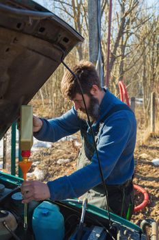 A man pours lubricating oil into the car. In the summer on the street next to the house.