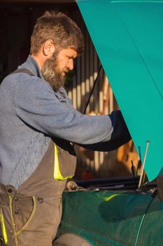 A man pours lubricating oil into the car. In the summer on the street next to the house.