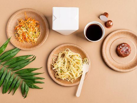 Eco friendly zero waste disposable tableware with pasta, salad and donut top view flat lay on brown background