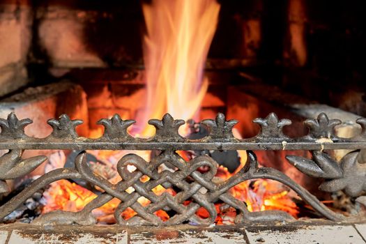 Cast-iron fireplace grille against the background of burning coals. Close up