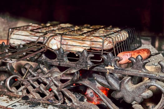 Grilling sausages and meat in a fireplace with a beautiful cast iron grate. Close up