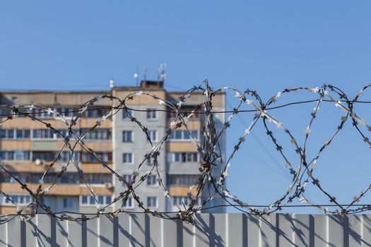 residential multi-storey building behind a fence with barbed wire at daylight, the concept of imprisonment, restriction of freedom, quarantine.