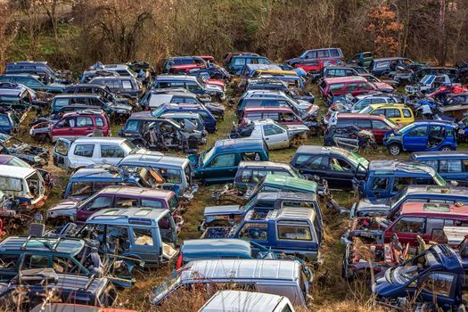 Many cars in a scrapyard with bonnets up and parts missing like tires