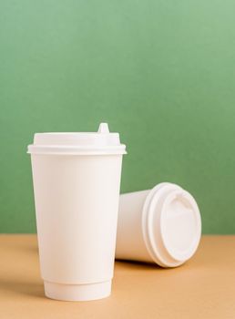 Eco friendly zero waste disposable tableware. White large takeaway paper coffee cups mock up on green and brown background