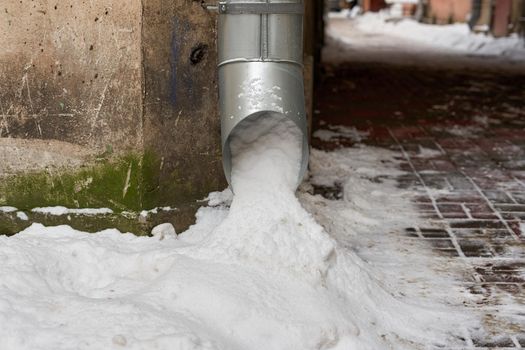 The metal drainpipe on the corner of the house is filled with snow. Close-up