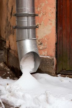 Drain pipe with frozen stream of water near brick wall of a cottage outdoors in winter