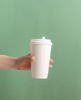 Eco friendly zero waste disposable tableware. Woman hand holding white large takeaway paper coffee cup mock up on green background