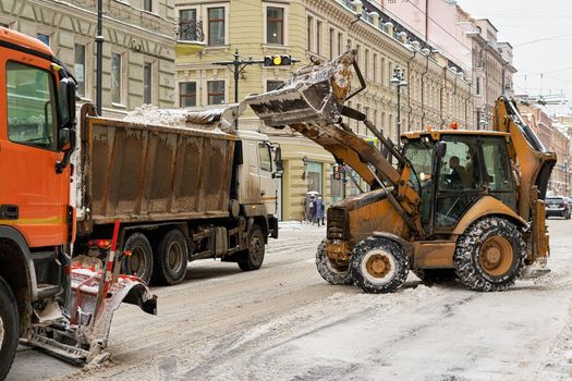 A tractor removes snow on the streets of a big European city. Close-up